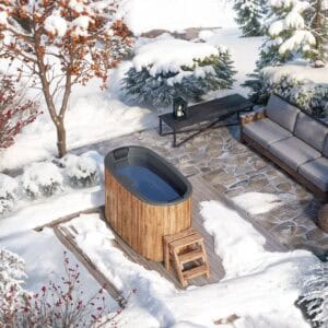 A cosy outdoor patio is covered in snow, featuring a Fibreglass Cold Plunge Tub for Two, a nearby barrel sauna with small steps, a cushioned sofa, a lantern-topped table, and surrounding snowy trees and bushes.