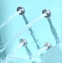 Four water jets are spraying streams of water into a light blue cold plunge tub or spa, creating splashes and shadows on the surface.